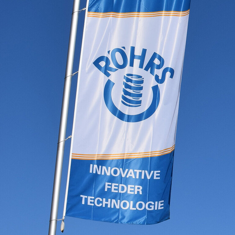 EIne große Fahne mit dem Logo der Firma Röhrs weht vor dem Verwaltungsgebäude in Sonthofen im Wind